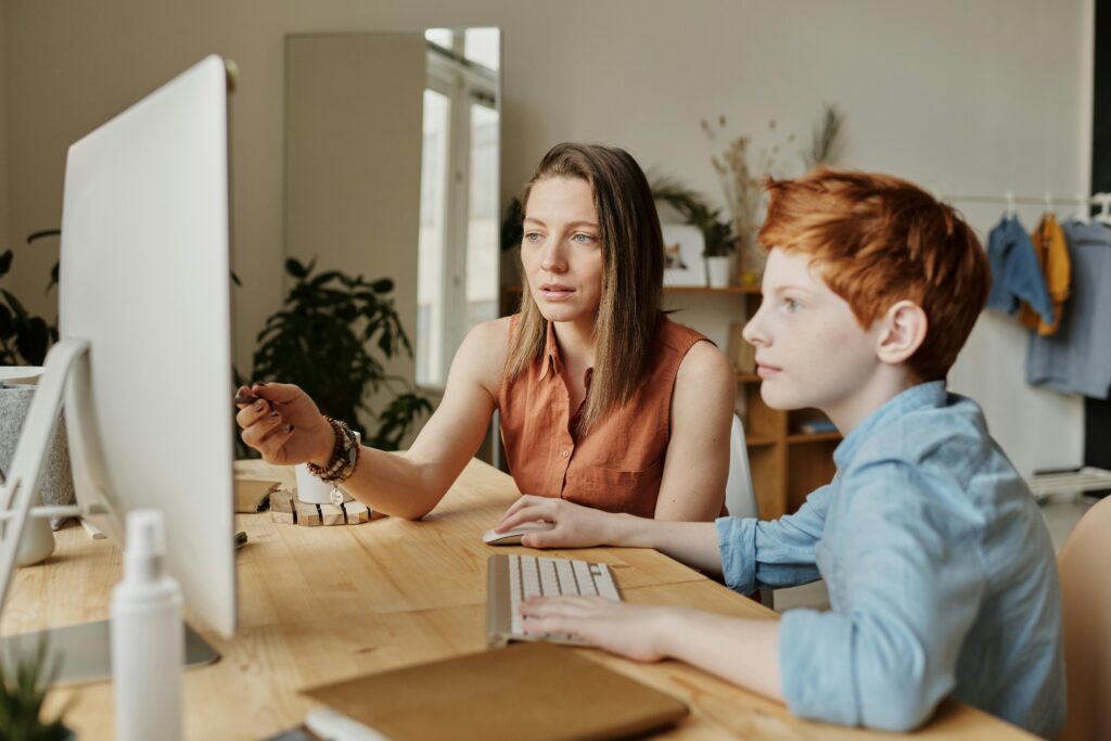 A mother and her son attentively engaged in online learning at home on a computer.